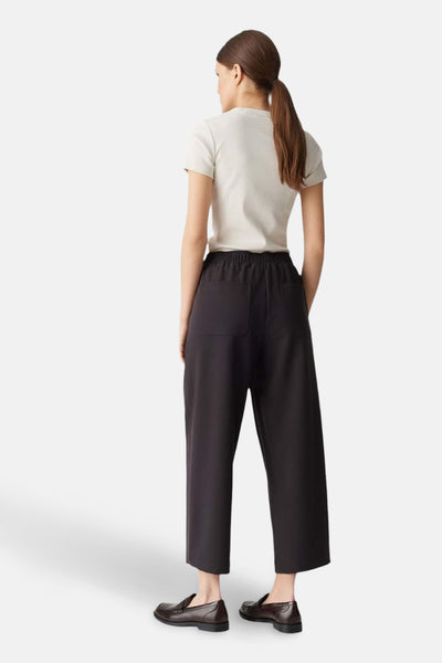 Pantalon brun par OPUS, avec taille élastique et deux poches arrière, porté avec un t-shirt crème et des mocassins.