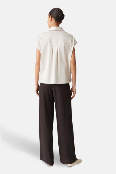 Chemisier écru de OPUS, avec un col classique et des plis au dos, porté avec un pantalon marron.