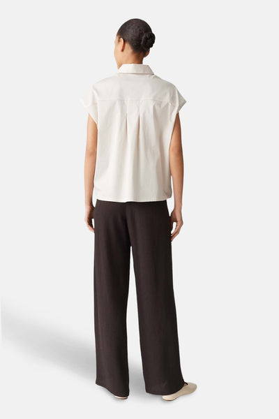 Chemisier écru de OPUS, avec un col classique et des plis au dos, porté avec un pantalon marron.