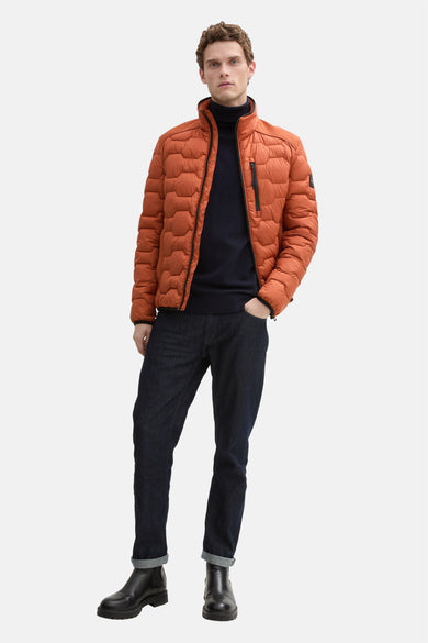 Veste courte orange par Tom Tailor, portée avec un col roulé bleu marine, un jean foncé et des bottines noires.