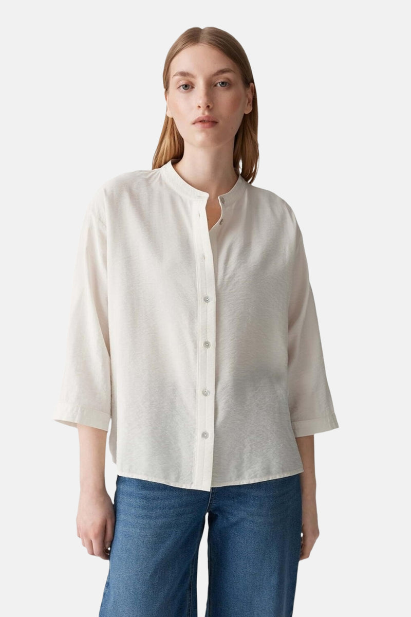 Chemise écru à manches longues par OPUS, avec boutons et col mao, portée avec un jean bleu.
