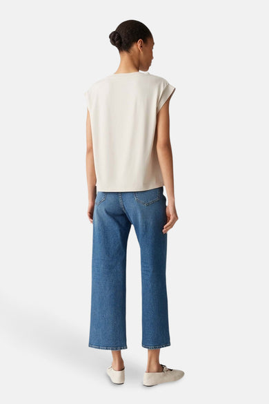 Blouse écrue sans manches par OPUS, portée avec un jean bleu taille haute et des chaussures plates.