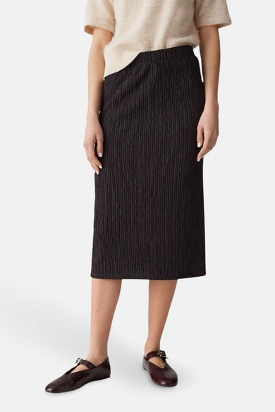 Jupe longue marron de OPUS avec une texture plissée, portée avec un pull beige et des chaussures plates marron.
