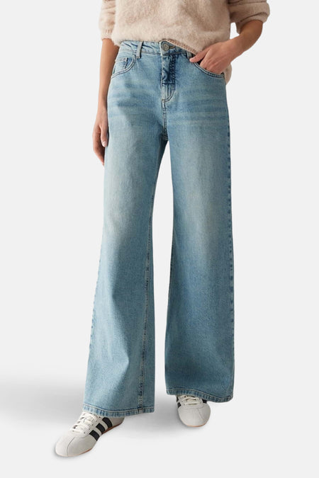 Jean droit en denim bleu clair par OPUS, coupe palazzo ample et chaussures de sport blanches.