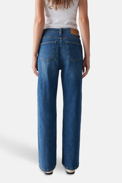 Jeans larges bleu foncé de OPUS, avec poches arrière et étiquette en cuir, portés avec un t-shirt blanc.