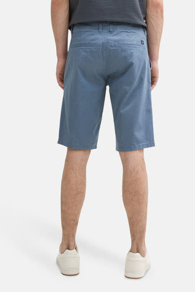 Short bleu de Tom Tailor, avec poches arrière, porté avec un t-shirt gris et des baskets blanches.