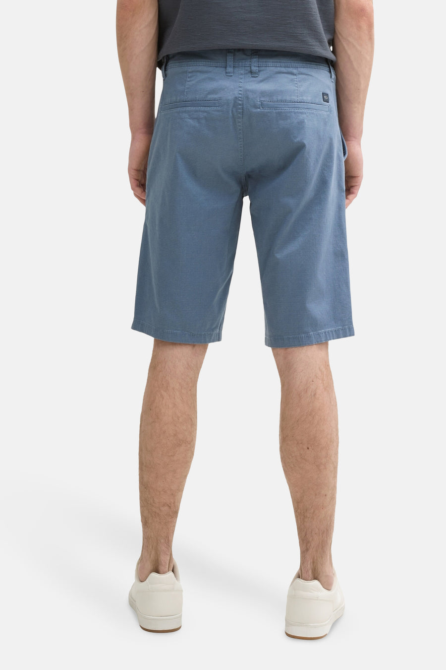 Short bleu de Tom Tailor, avec poches arrière, porté avec un t-shirt gris et des baskets blanches.