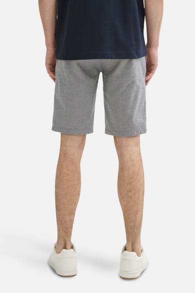 Short bleu de Tom Tailor, à motif subtil, porté avec un t-shirt bleu marine et des baskets beiges, vue de dos.
