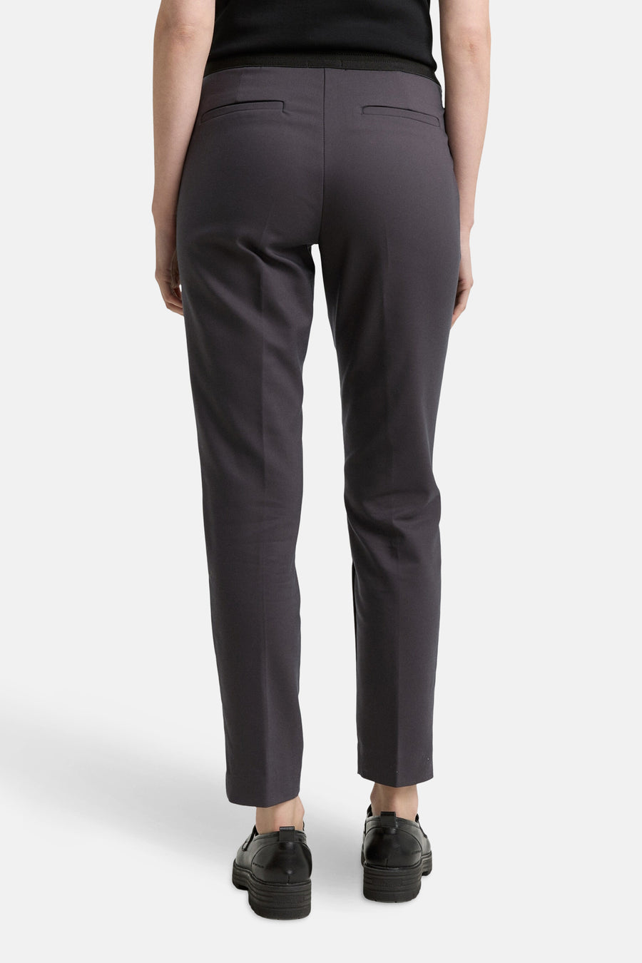 Grijze broek van Tom Tailor, met paspelzakken achter, gedragen met zwarte schoenen met dikke zolen.