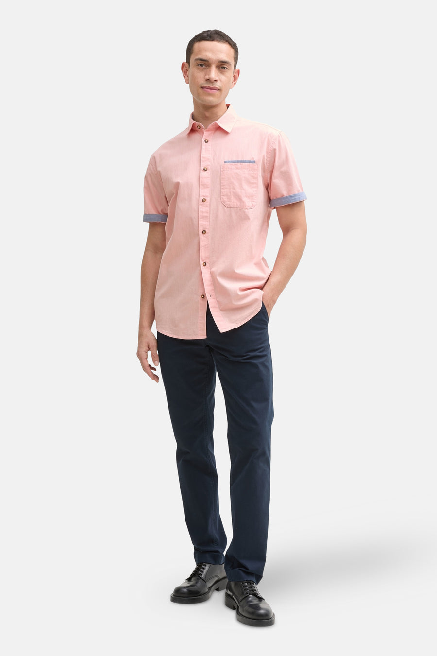 Chemise corail à manches courtes de Tom Tailor, avec poche poitrine et détails contrastés aux manches, portée avec un pantalon bleu marine.