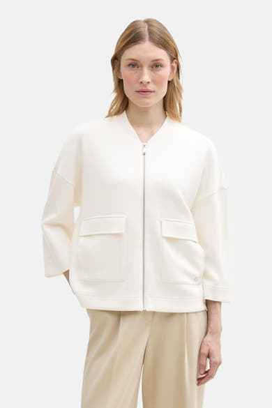 Witte bodywarmer van Tom Tailor, open gedragen met een beige wijde broek en een zwarte leren tas.
