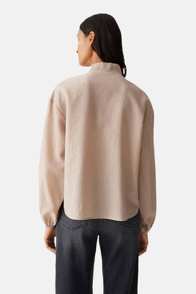 Beige blouse met lange mouwen van OPUS, getextureerd, met een opstaande kraag, gedragen met een verbleekte spijkerbroek.