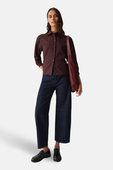 Chemise à manches longues bordeaux par OPUS, portée avec un jean ample et un sac fourre-tout bordeaux.