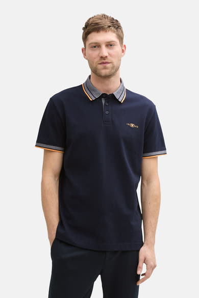 Donkerblauwe polo met korte mouwen van Tom Tailor, met strepen op de kraag en mouwen, gedragen met een marineblauwe broek en zwarte schoenen.