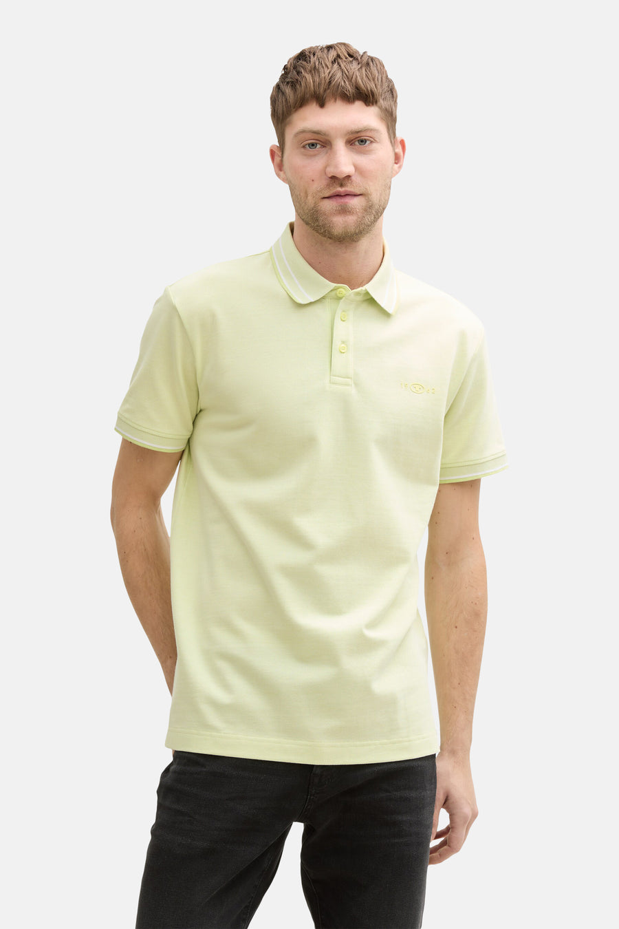 Groen poloshirt met korte mouwen van Tom Tailor, met witte randen aan de mouwen en kraag, gedragen met een zwarte jeans.