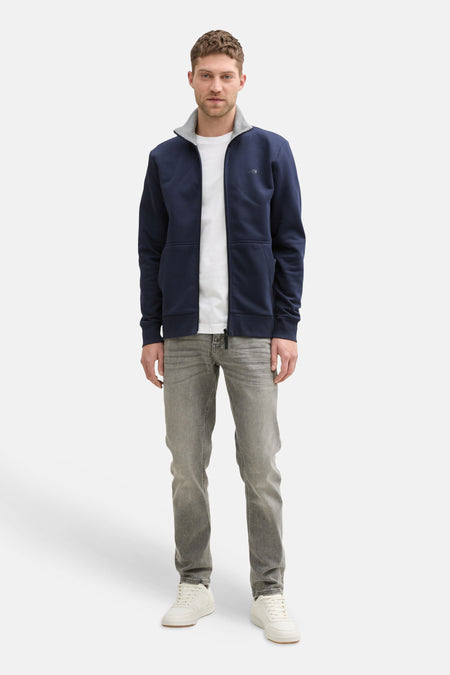 Gilet bleu marine Tom Tailor à col montant, porté par un mannequin avec un jean gris et des baskets blanches.