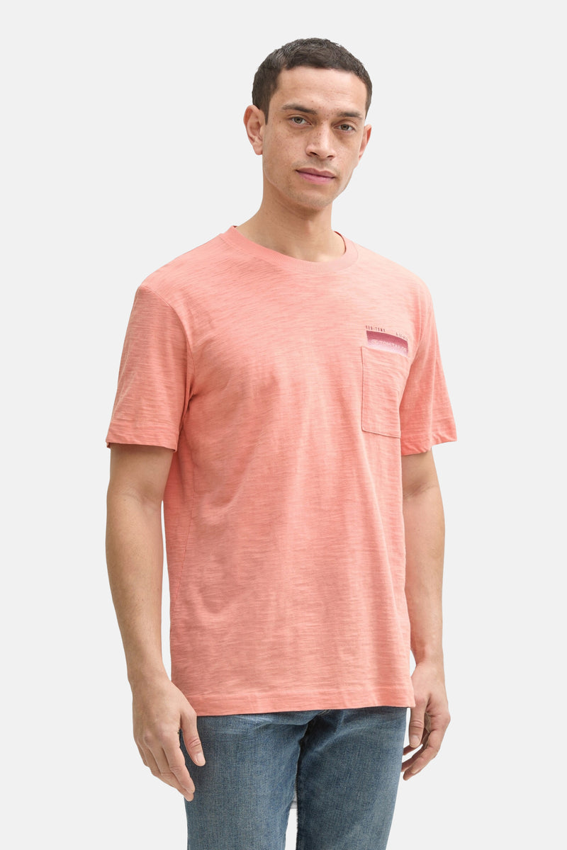 Koraalkleurig T-shirt met korte mouwen van Tom Tailor, met borstzak en gedragen met een blauwe jeans en witte sneakers.