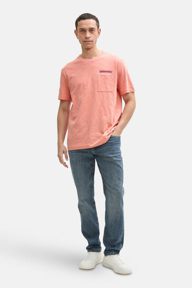 T-shirt corail à manches courtes de Tom Tailor, avec poche poitrine et porté avec un jean bleu et des baskets blanches.
