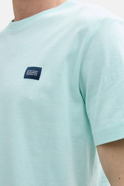 T-shirt turquoise à manches courtes de Tom Tailor, avec un écusson bleu marine sur la poitrine.
