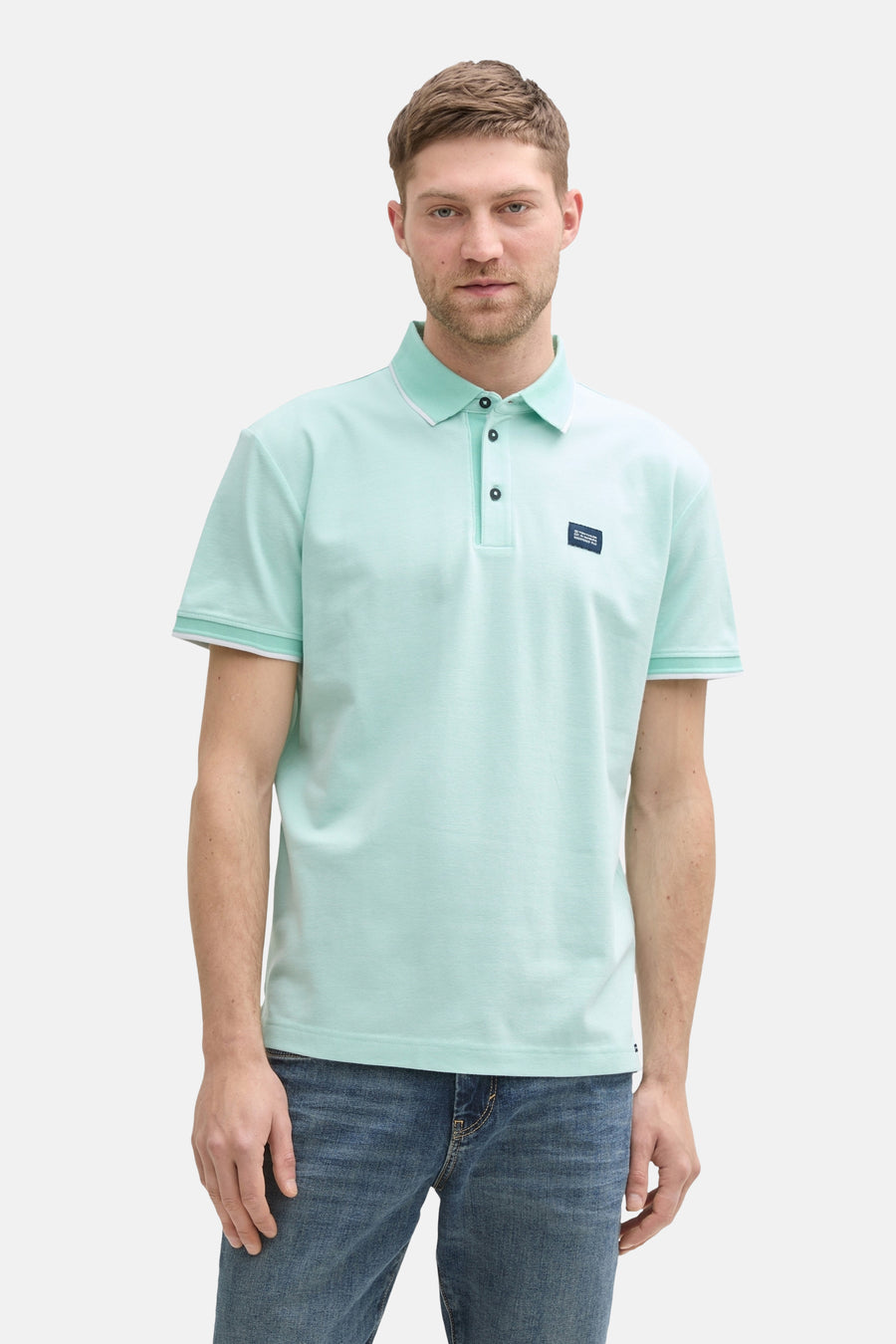 Groen poloshirt met korte mouwen van Tom Tailor, met witgekleurde kraag en mouwen, gedragen met een spijkerbroek.