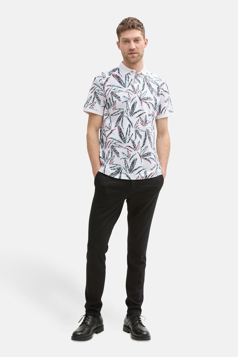 Polo multicolore à manches courtes de Tom Tailor, avec imprimé feuillage, porté avec un pantalon noir et des chaussures noires.