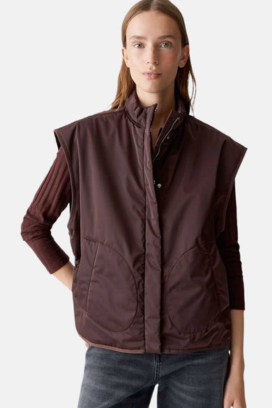 Rood mouwloos vest van OPUS, met trekkoord in de taille en gedragen over een bruine trui en een donkere jeans.