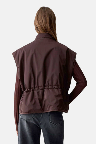 Veste sans manches rouge par OPUS, avec cordon de serrage à la taille et portée sur un pull marron et un jean foncé.
