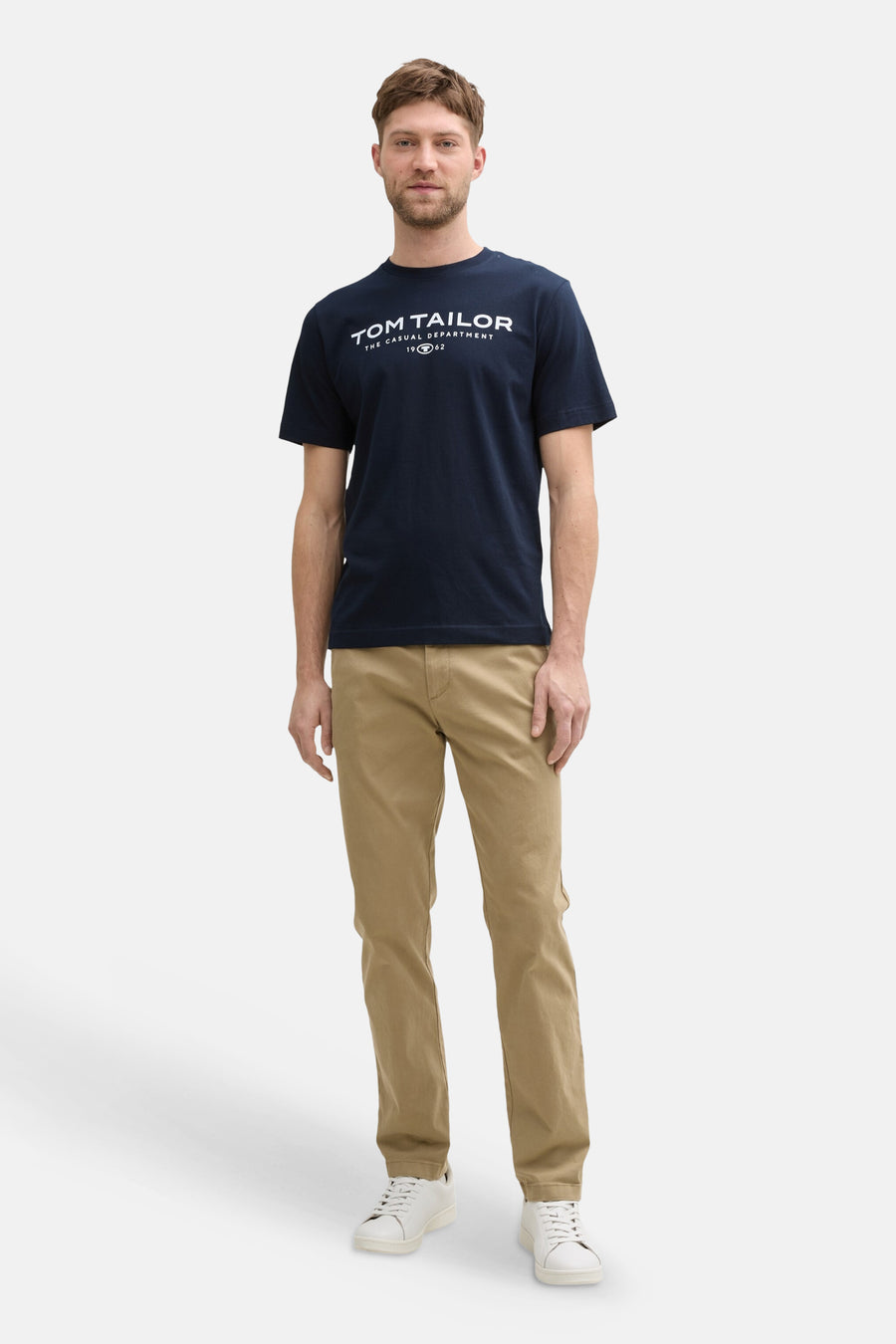 Navy blue short-sleeve T-shirt by Tom Tailor with white logo print, worn with khaki pants and white sneakers in full-length front view.