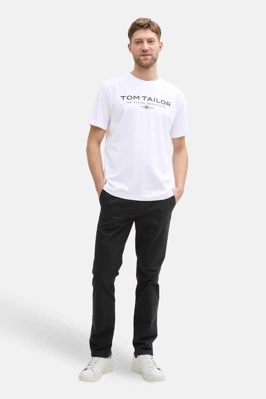 White short-sleeve T-shirt by Tom Tailor with black logo print, worn with black pants and white sneakers, full-body front view