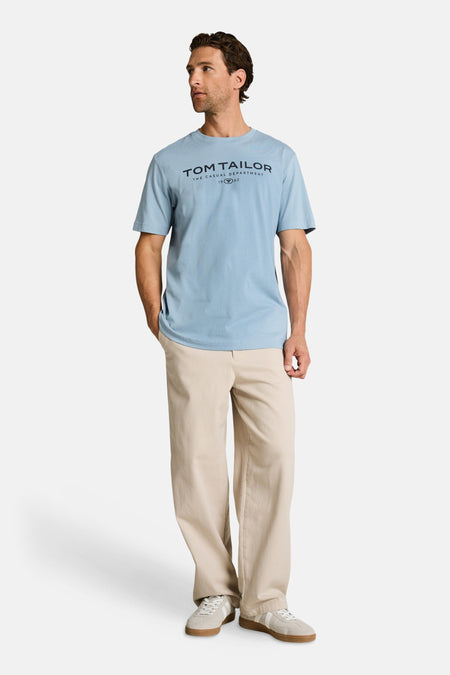 T-shirt bleu clair de Tom Tailor avec inscription, porté avec un pantalon beige et des baskets.