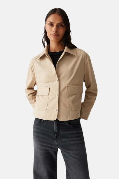 Veste courte beige van OPUS, avec des poches plaquées, portée sur un haut noir et un jean gris.