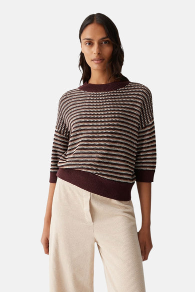 Pull à col rond marron, par OPUS, à rayures horizontales beiges et marron foncé, porté avec un pantalon beige côtelé.