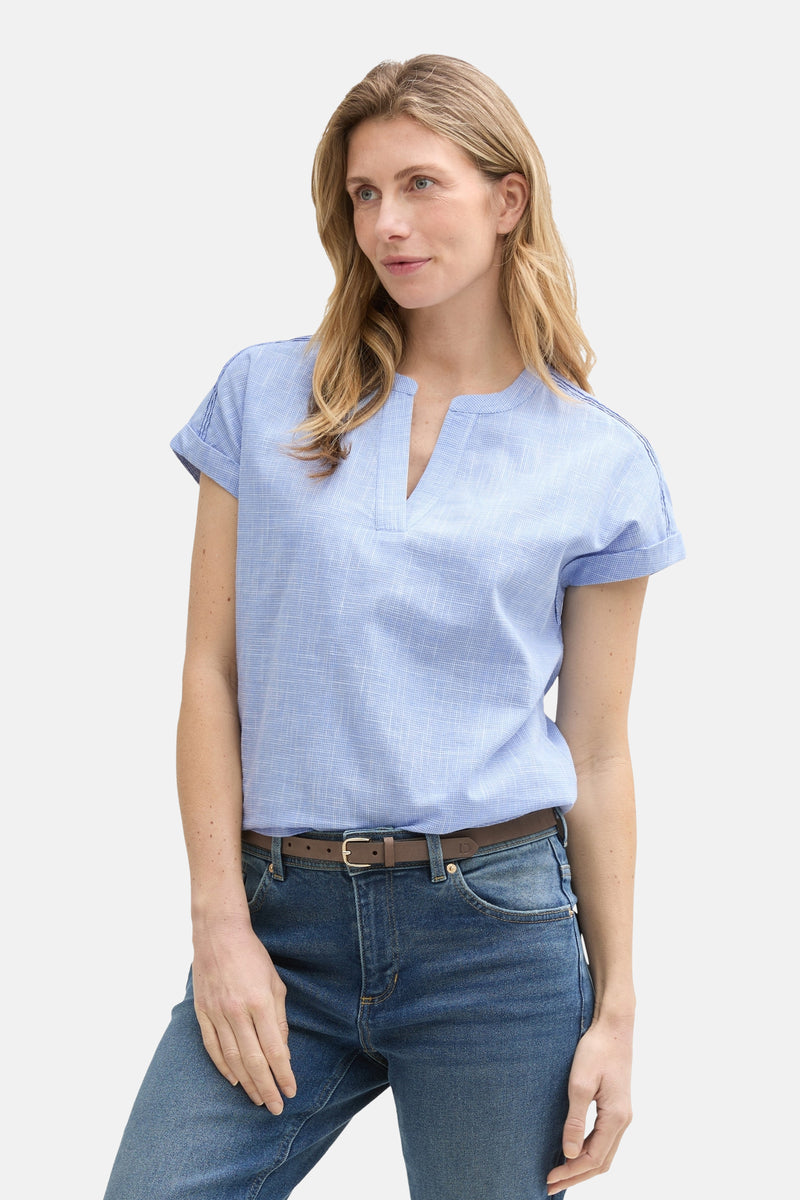 Blouse à manches courtes bleue de Tom Tailor, avec col en V et manches à revers, portée avec un jean et une ceinture marron.