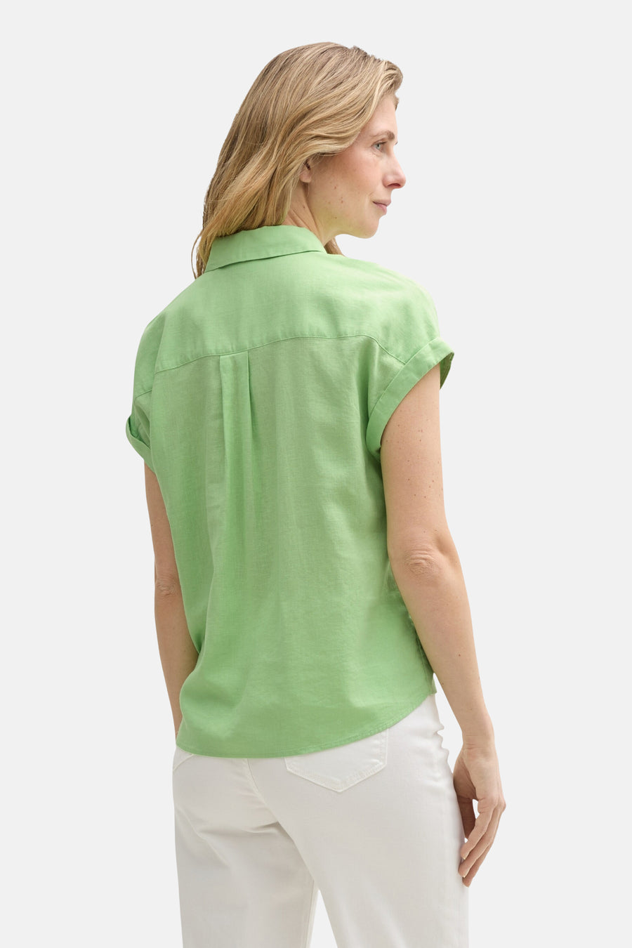 Chemisier vert à manches courtes de Tom Tailor, avec des plis au dos, porté avec un pantalon blanc.
