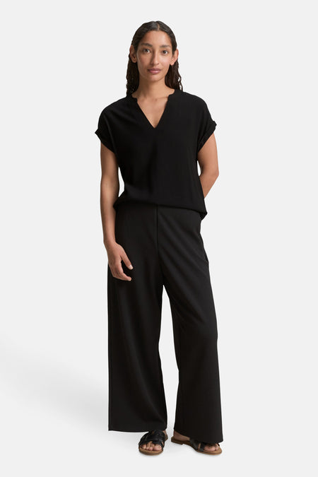 Zwart blouse met korte mouwen van Tom Tailor, gedragen met een zwarte wijde broek en sandalen.