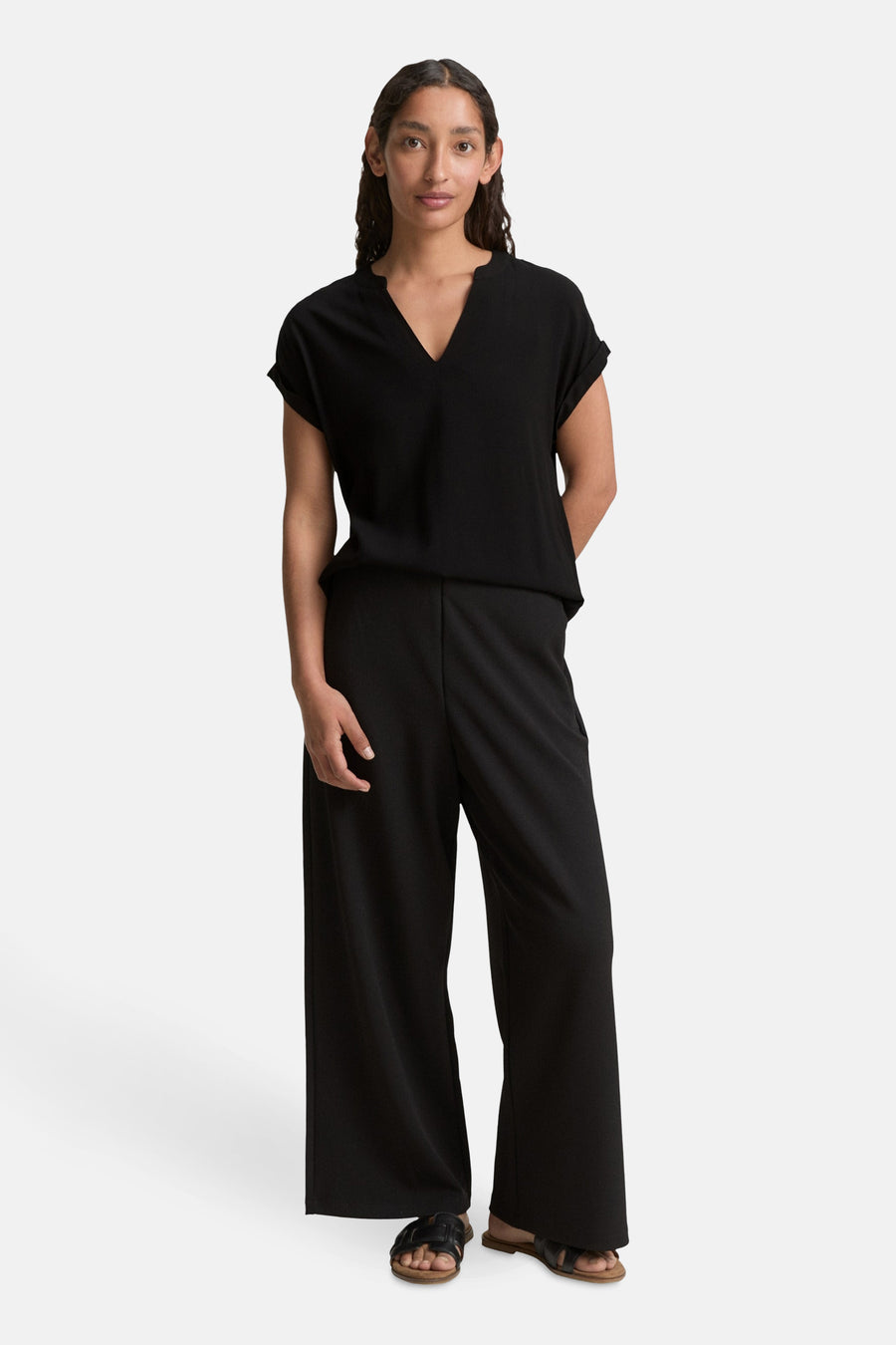 Blouse noire à manches courtes de Tom Tailor, portée avec un pantalon large noir et des sandales.