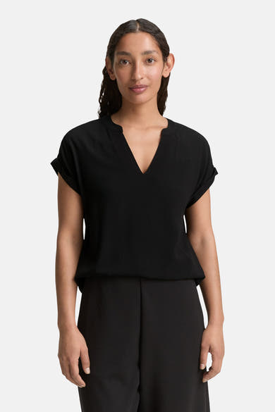 Blouse noire à manches courtes de Tom Tailor, avec un col en V, portée avec un pantalon noir.