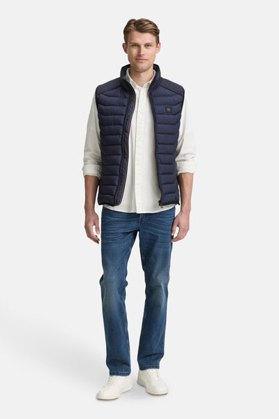 Veste sans manches bleue de Tom Tailor, portée sur une chemise claire et un jean bleu.