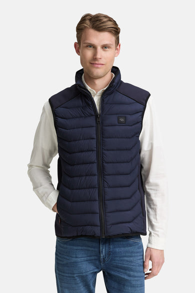 Veste sans manches bleu par Tom Tailor, avec fermeture éclair visible, portée sur une chemise blanche et un jean bleu.