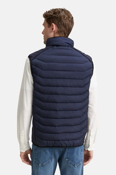 Veste sans manches bleu de Tom Tailor, avec matelassage horizontal, portée sur une chemise blanche et un jean.