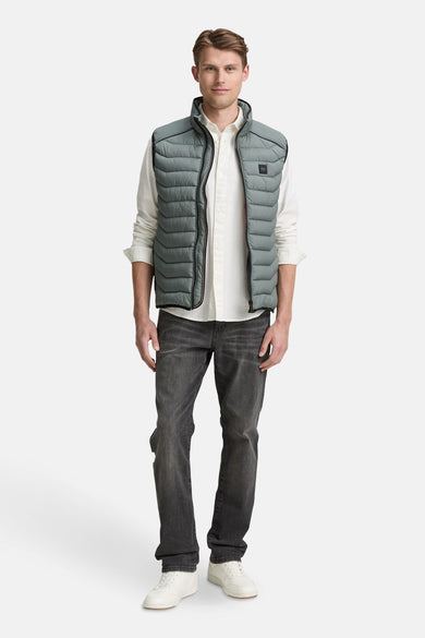 Veste sans manches verte par Tom Tailor, portée sur une chemise blanche avec un jean foncé et des baskets blanches.