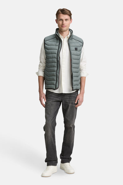 Veste sans manches verte par Tom Tailor, portée sur une chemise blanche avec un jean foncé et des baskets blanches.