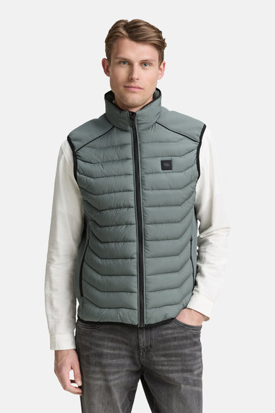 Veste sans manches verte de Tom Tailor, matelassée et portée sur une chemise blanche avec un jean gris.