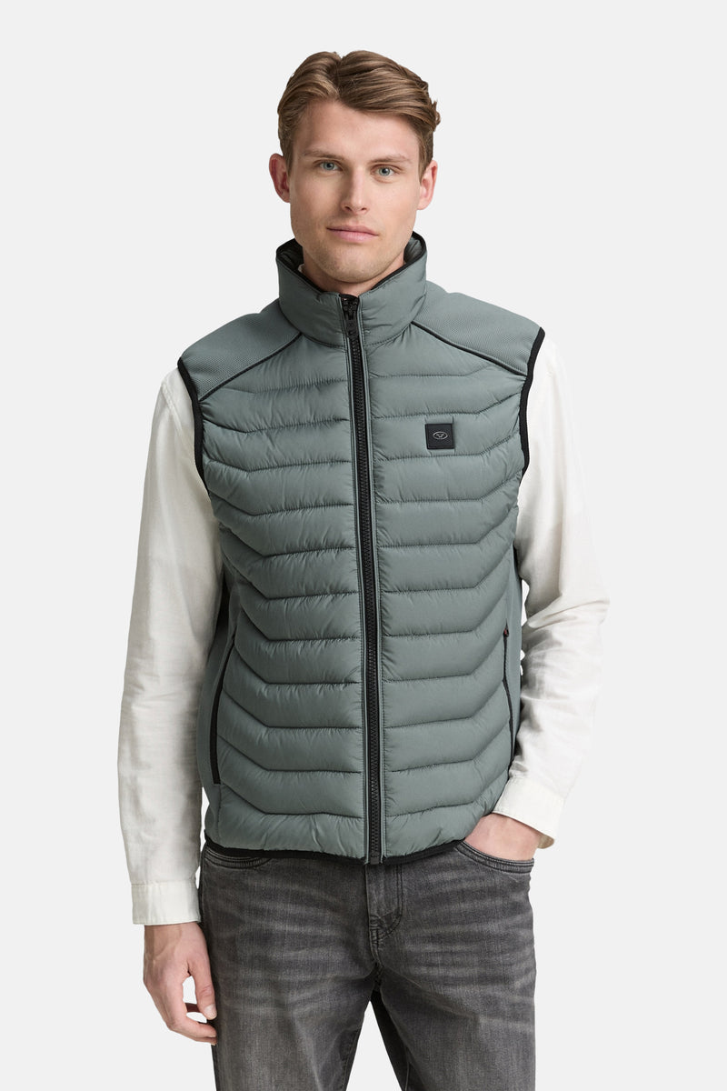 Veste sans manches verte de Tom Tailor, matelassée et portée sur une chemise blanche avec un jean gris.