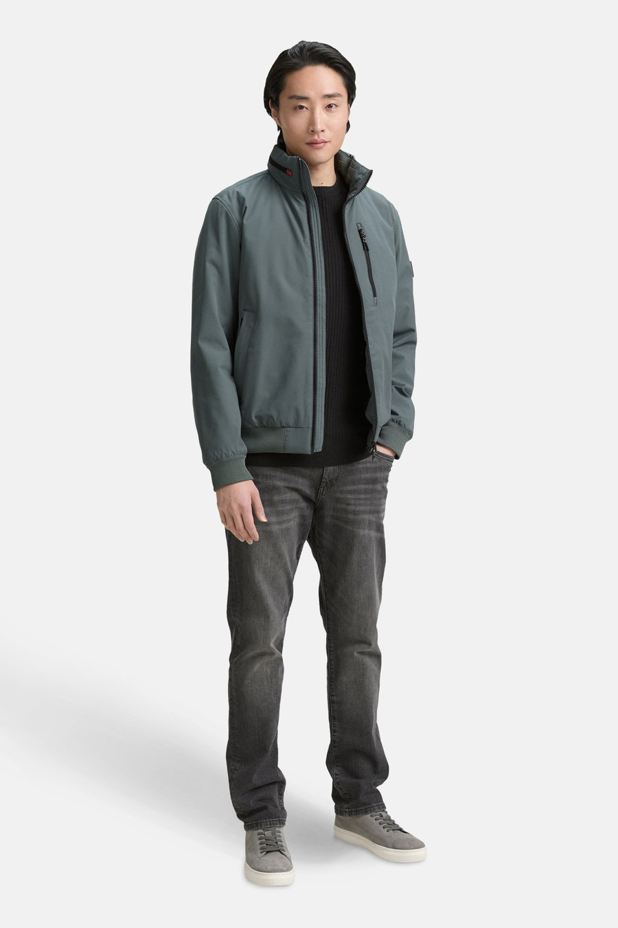 Veste courte verte par Tom Tailor, portée avec un pull noir et un jean délavé, avec des chaussures grises.