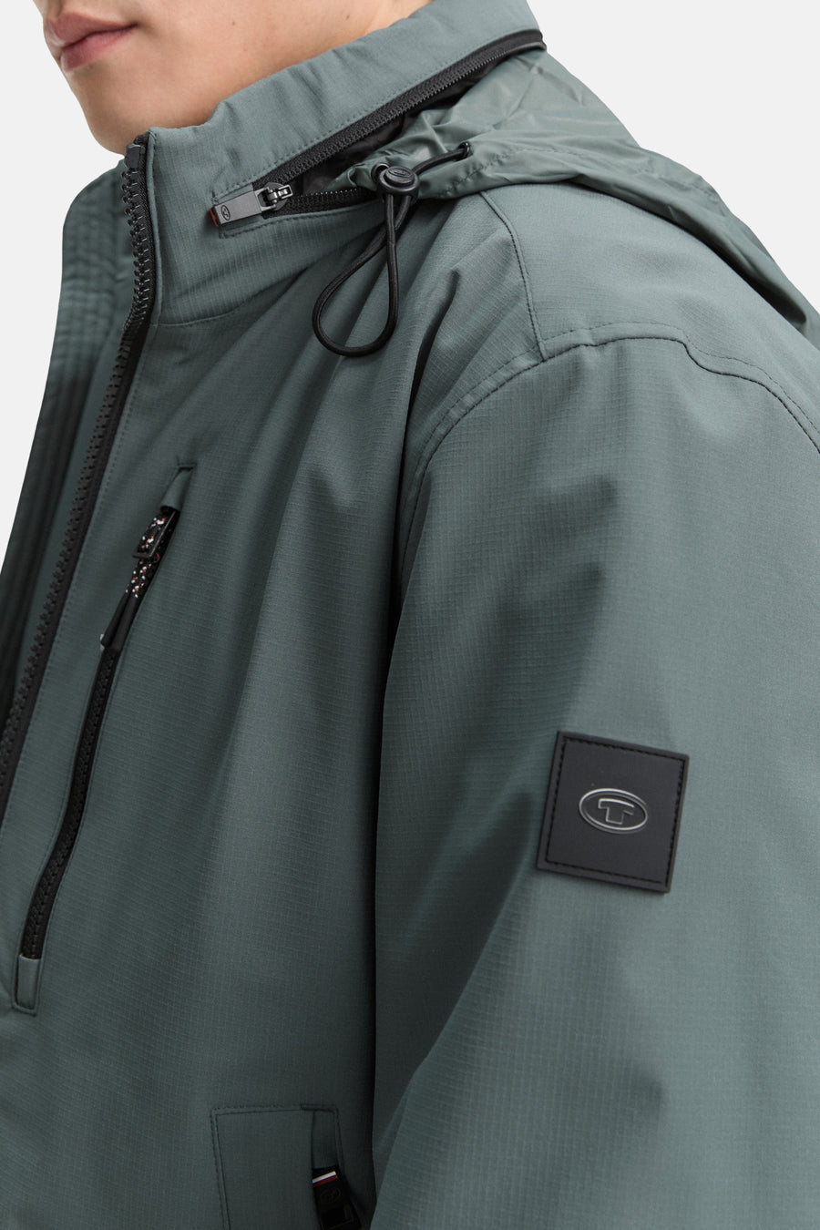 Veste courte verte de Tom Tailor, avec capuche et fermeture éclair noire, détail du logo de la marque sur la manche.