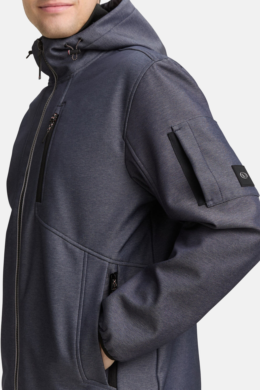 Korte blauwe jas van Tom Tailor, met capuchon, ritszakken en logopatch op de mouw.