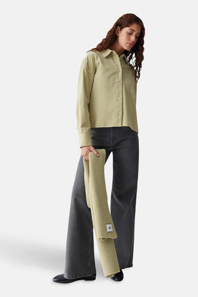Écharpe verte en tricot côtelé de OPUS, tenue par une femme portant une chemise et un jean gris.