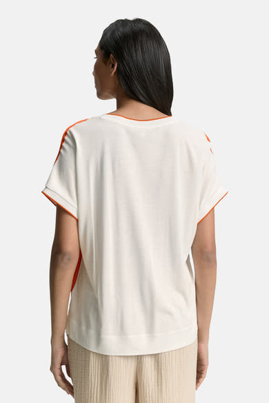 Chemisier à manches courtes multicolore de Tom Tailor, avec ourlet orange vif et porté avec un pantalon couleur crème.
