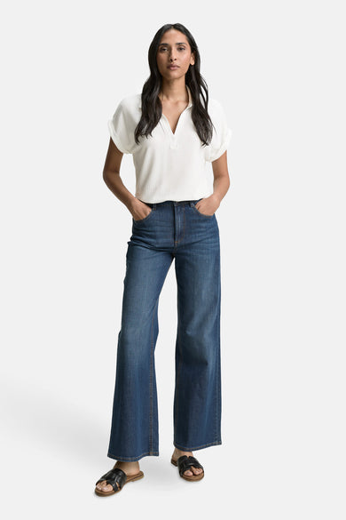 Polo blanc à manches courtes de Tom Tailor, porté avec un jean évasé bleu et des sandales noires.

